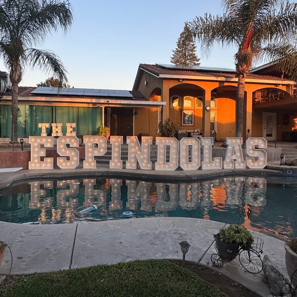Light-up marquee letters spelling a family name beside a pool at sunset
