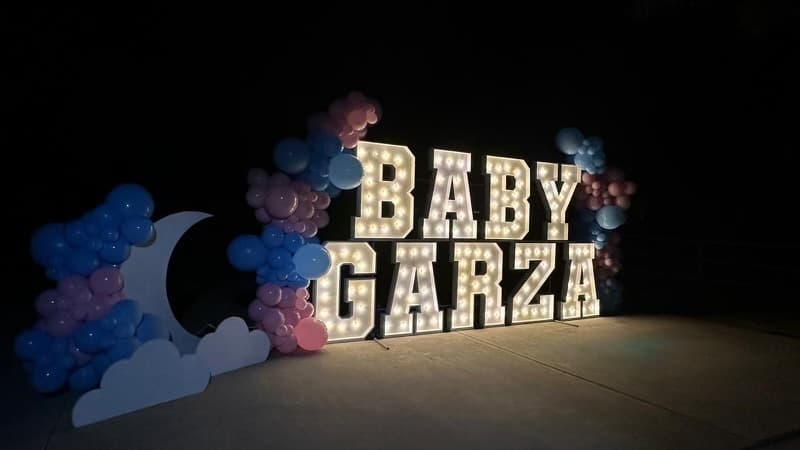 Light-up marquee letters spelling a custom name with pink and blue balloon decor at a baby shower