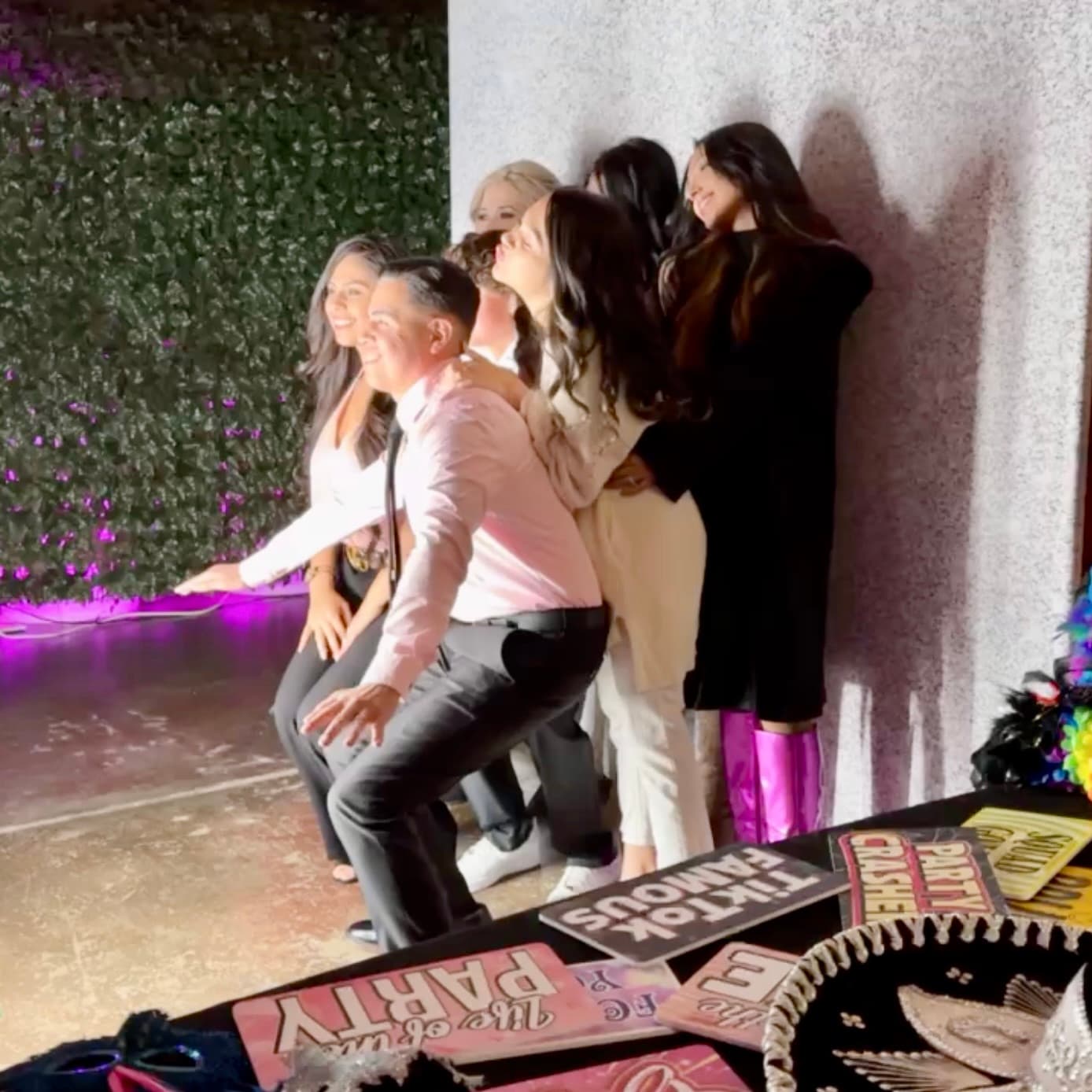 Guests posing at a photo booth with props and a hedge backdrop